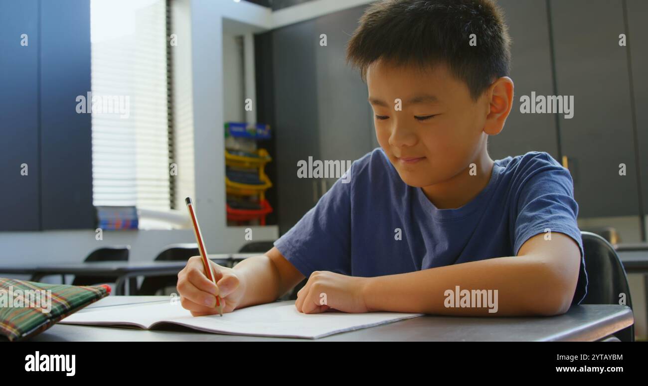 Front view of attentive Asian schoolboy studying at desk in classroom ...