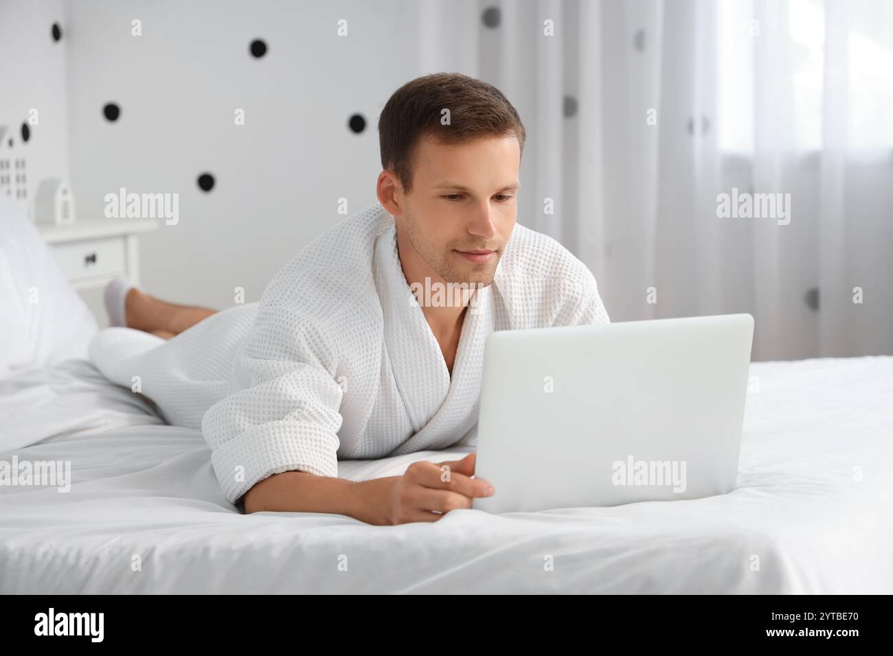 Young man in bathrobe using laptop on bed at home Stock Photo