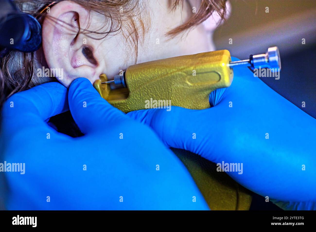 beautician in blue gloves creates a hole in the ears with a special tool. Ear piercing Style and beauty Stock Photo