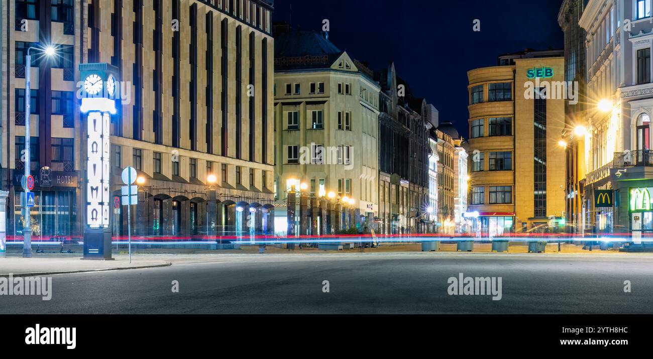 Nighttime street view in Old Riga with historic buildings, modern lights, and light trails from passing vehicles, creating a dynamic urban scene. Latv Stock Photo