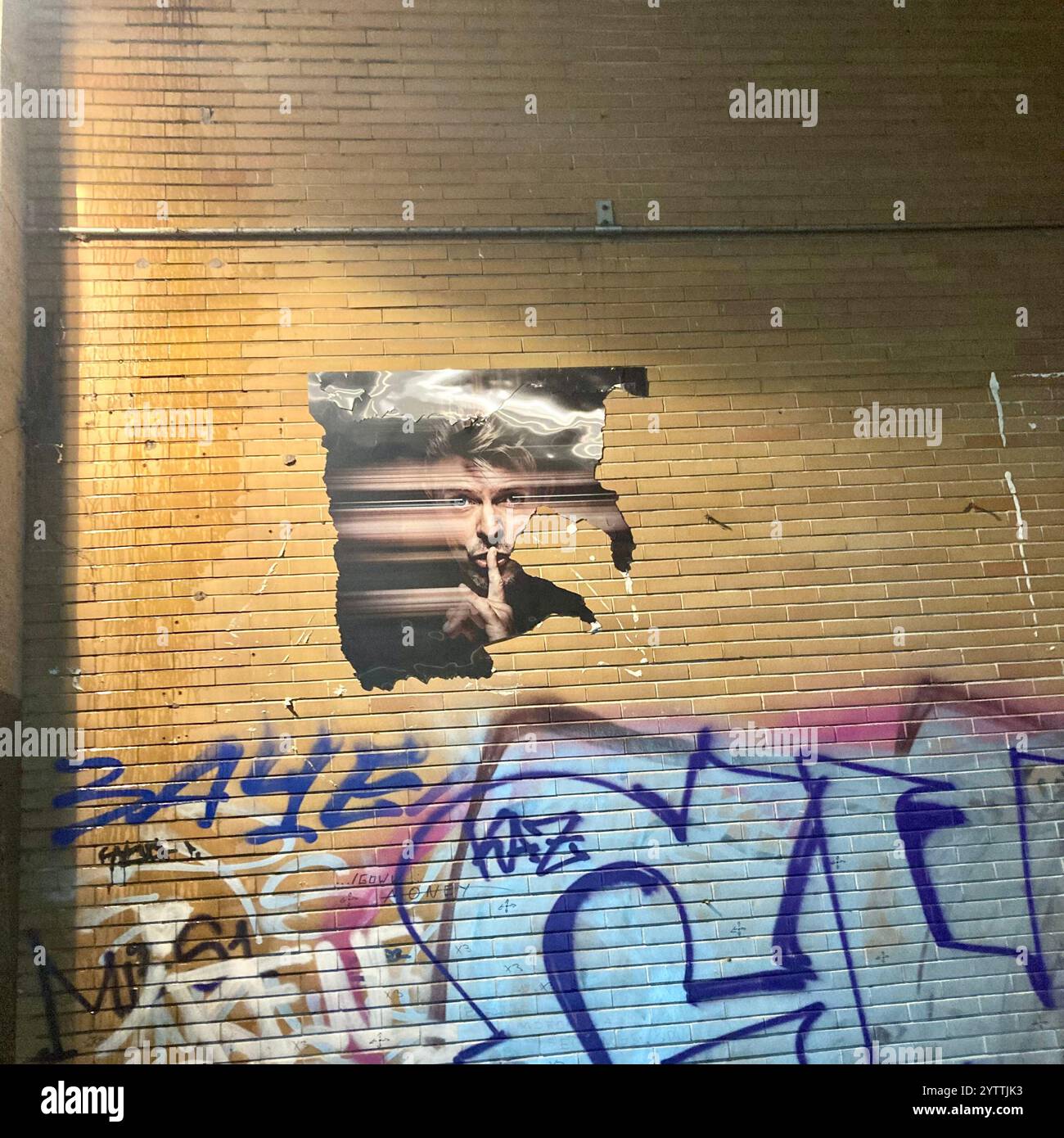 A torn photo poster of the late David Bowie with a finger in front of his mouth going shush on a wall in Berlin Stock Photo