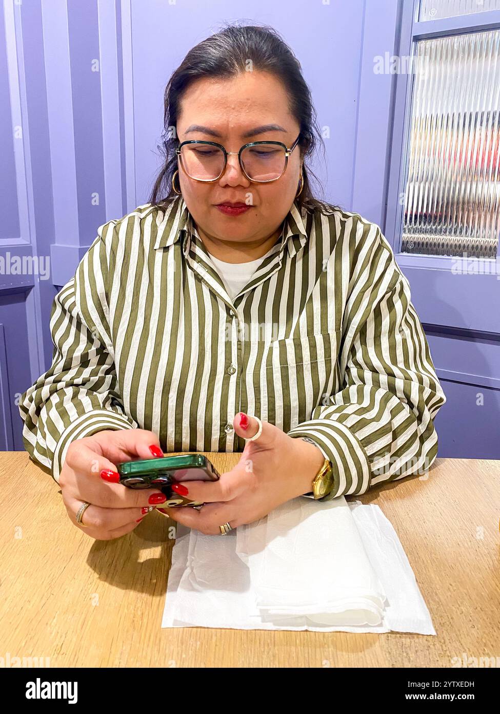 A lady sits at a table in a restaurant with her mobile phone. - Smartphone Captured Stock Image