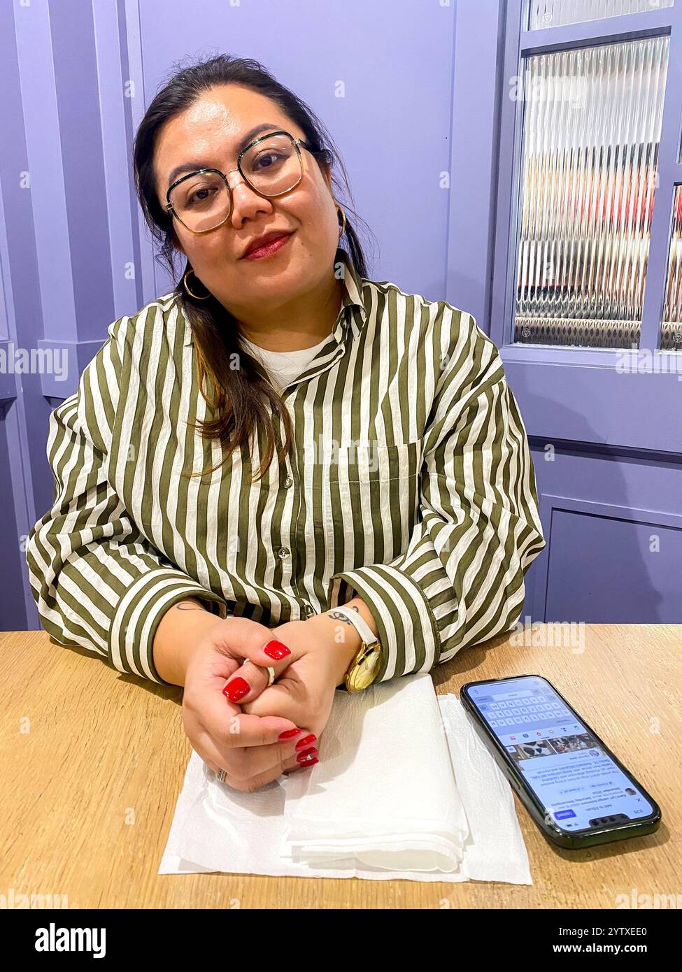 A lady sits at a table in a restaurant with her mobile phone. - Smartphone Captured Stock Image