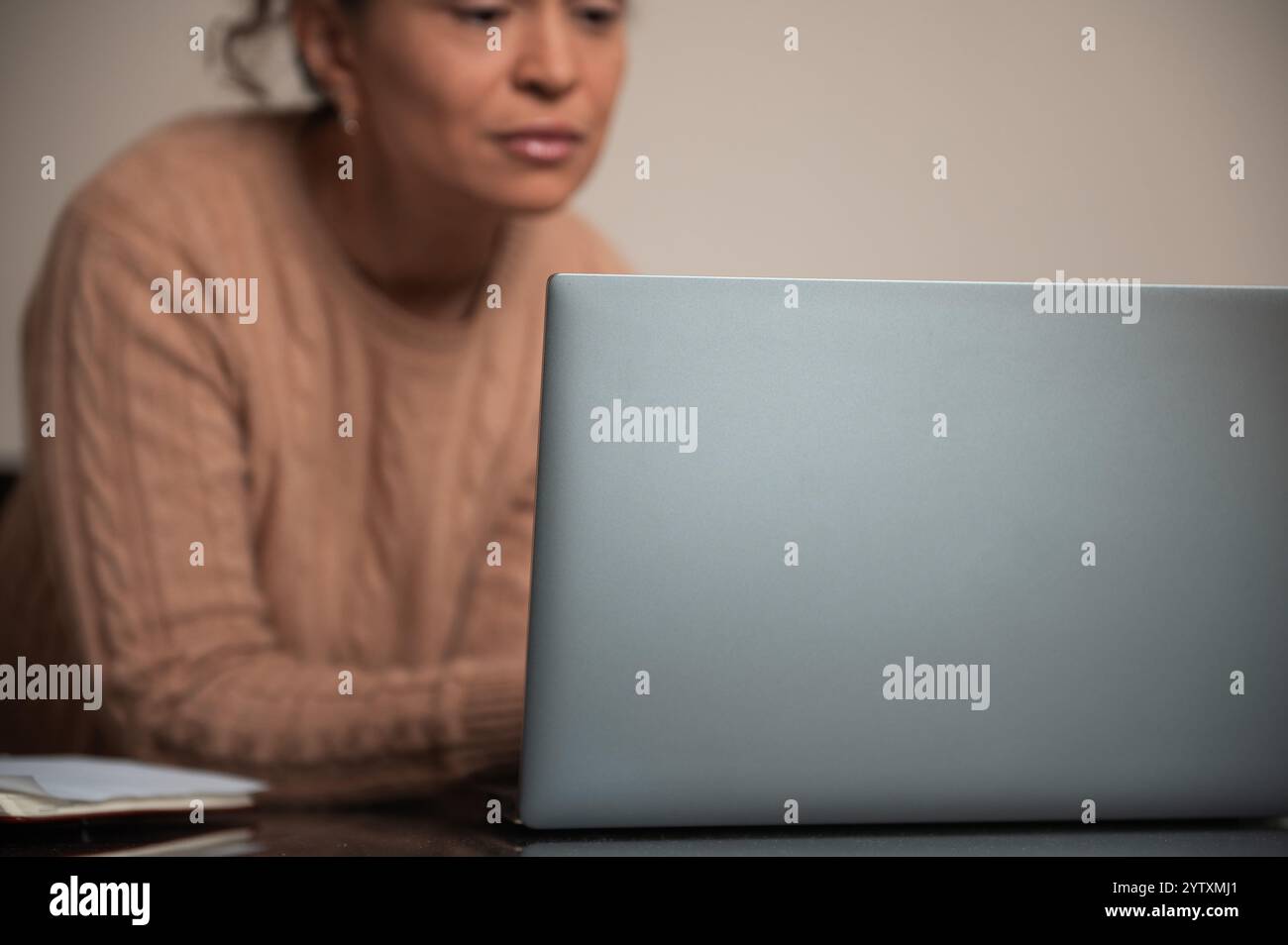 A woman in a sweater intently works on her laptop at home ...