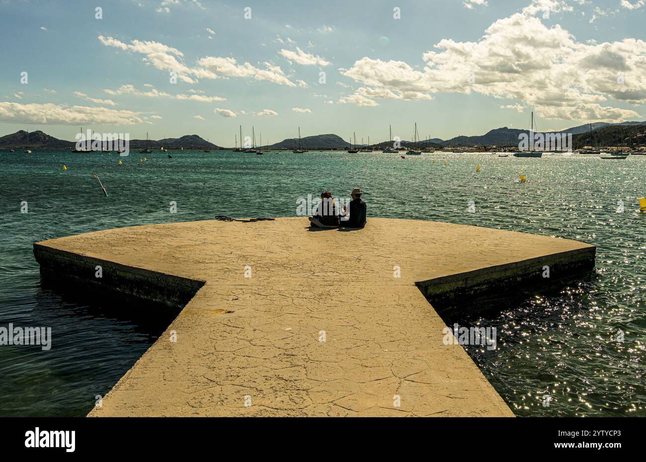 Sitzendes Paar auf dem Bootssteg mit Blick auf die Bucht von Port de Pollenca, Mallorca, Spanien Stock Photo