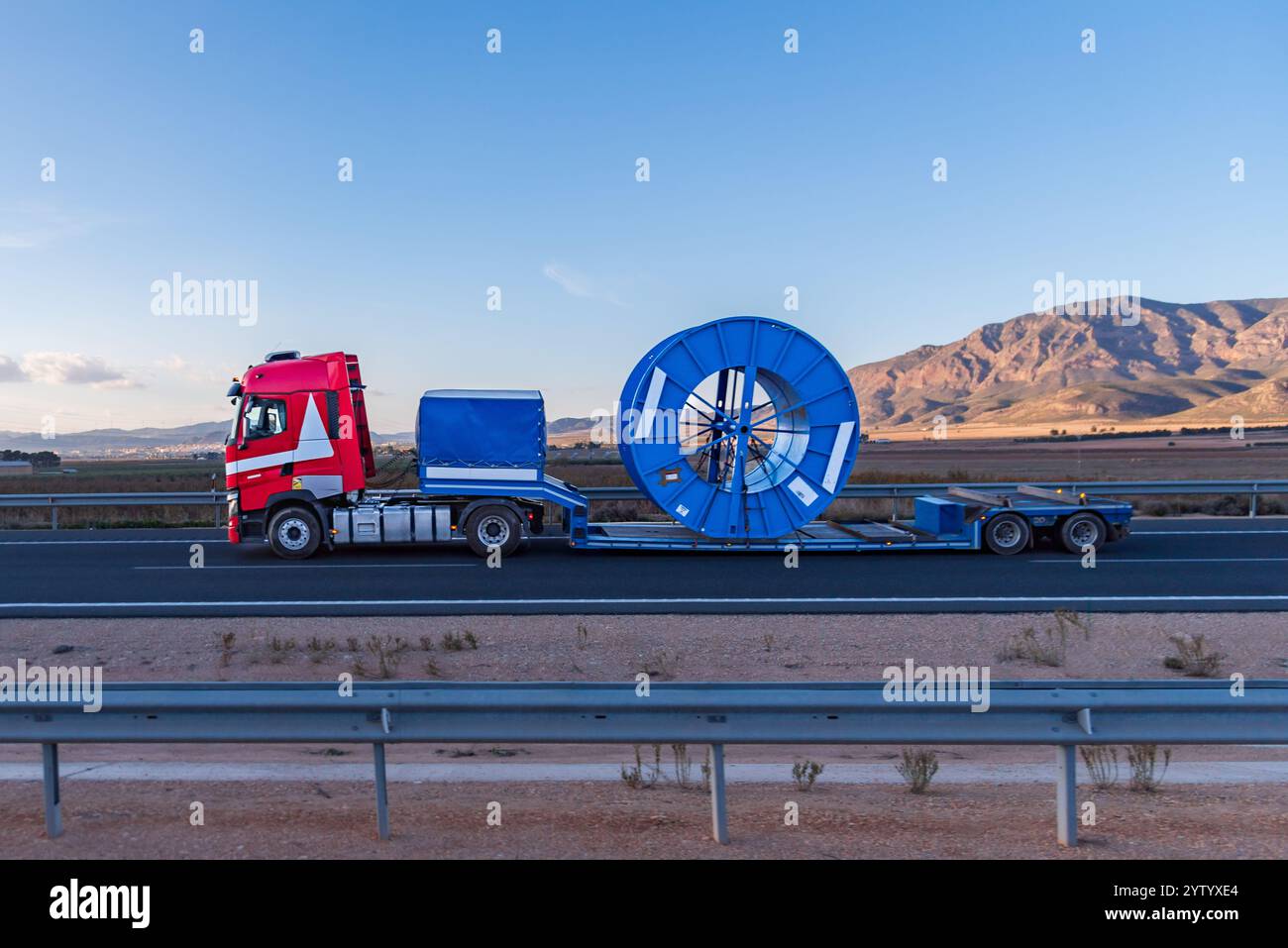 Truck with a semi-trailer designed for special transports, carrying a large coil used for transporting oversized cables. Stock Photo