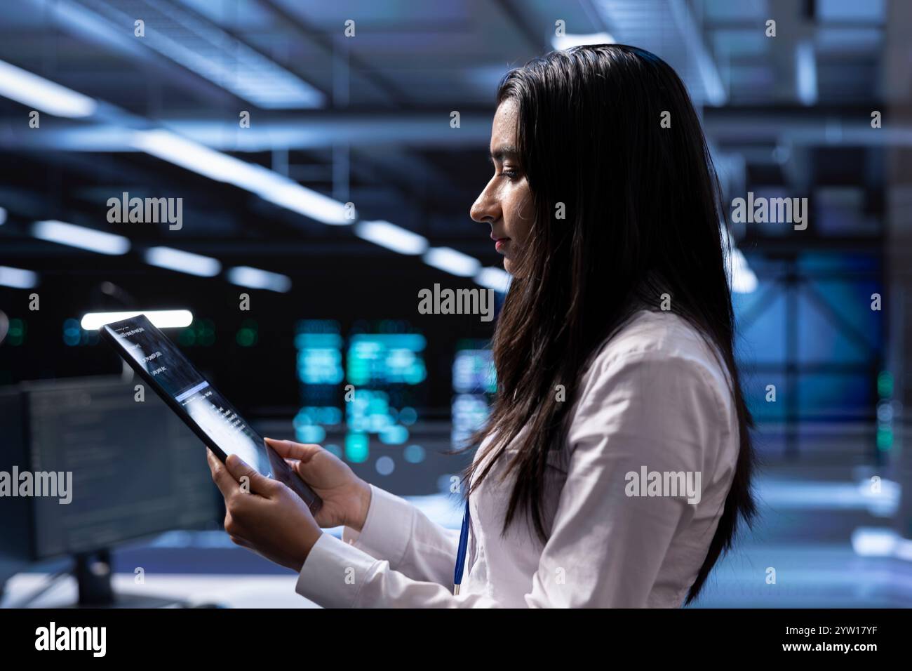 Engineer in data center updating systems to keeps performance up and protect servers from easily exploitable software vulnerabilities. Employee looking for errors causing servers to slow down using tablet Stock Photo