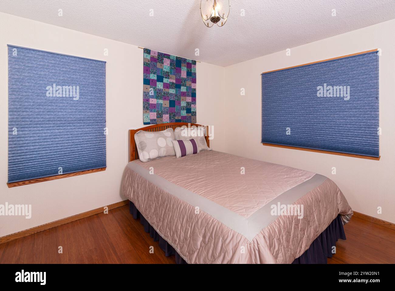 interior of bedroom with queen size bed atop wooden bamboo floors and decor hanging on wall above bed Stock Photo