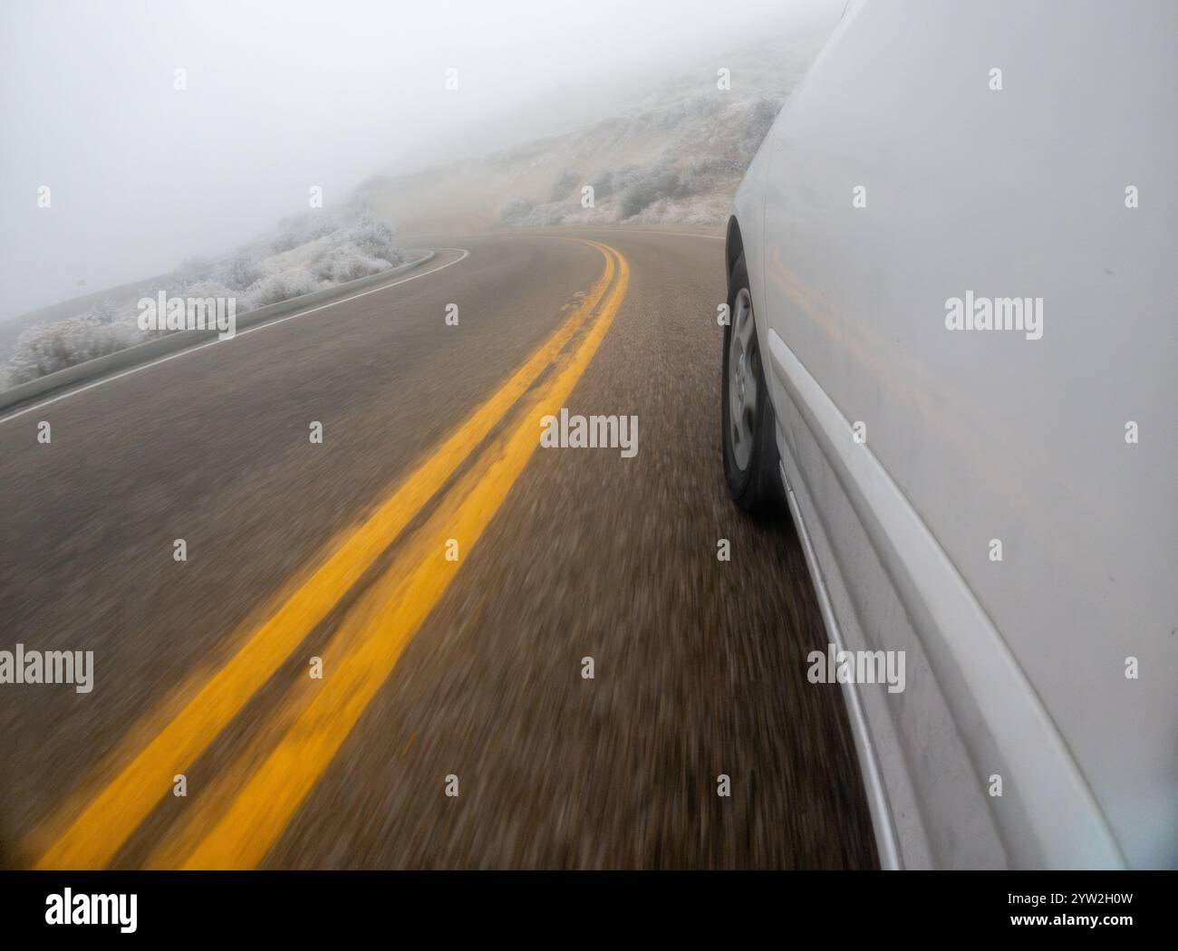 A car is driving down a road with yellow lines. The road is wet and the car is going fast Stock Photo