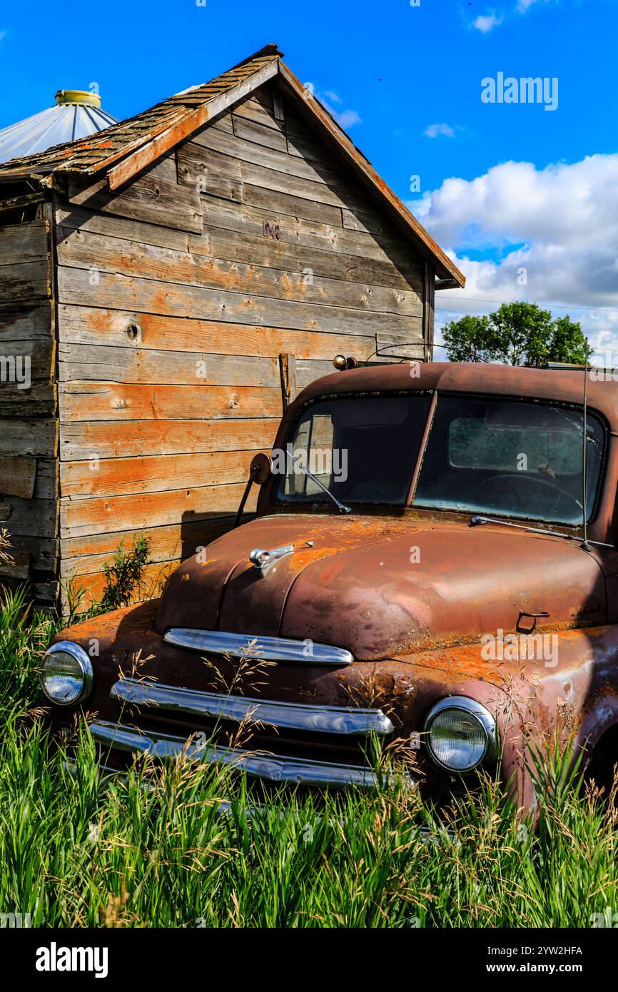 An old truck is parked in a field next to a barn. The truck is rusted ...