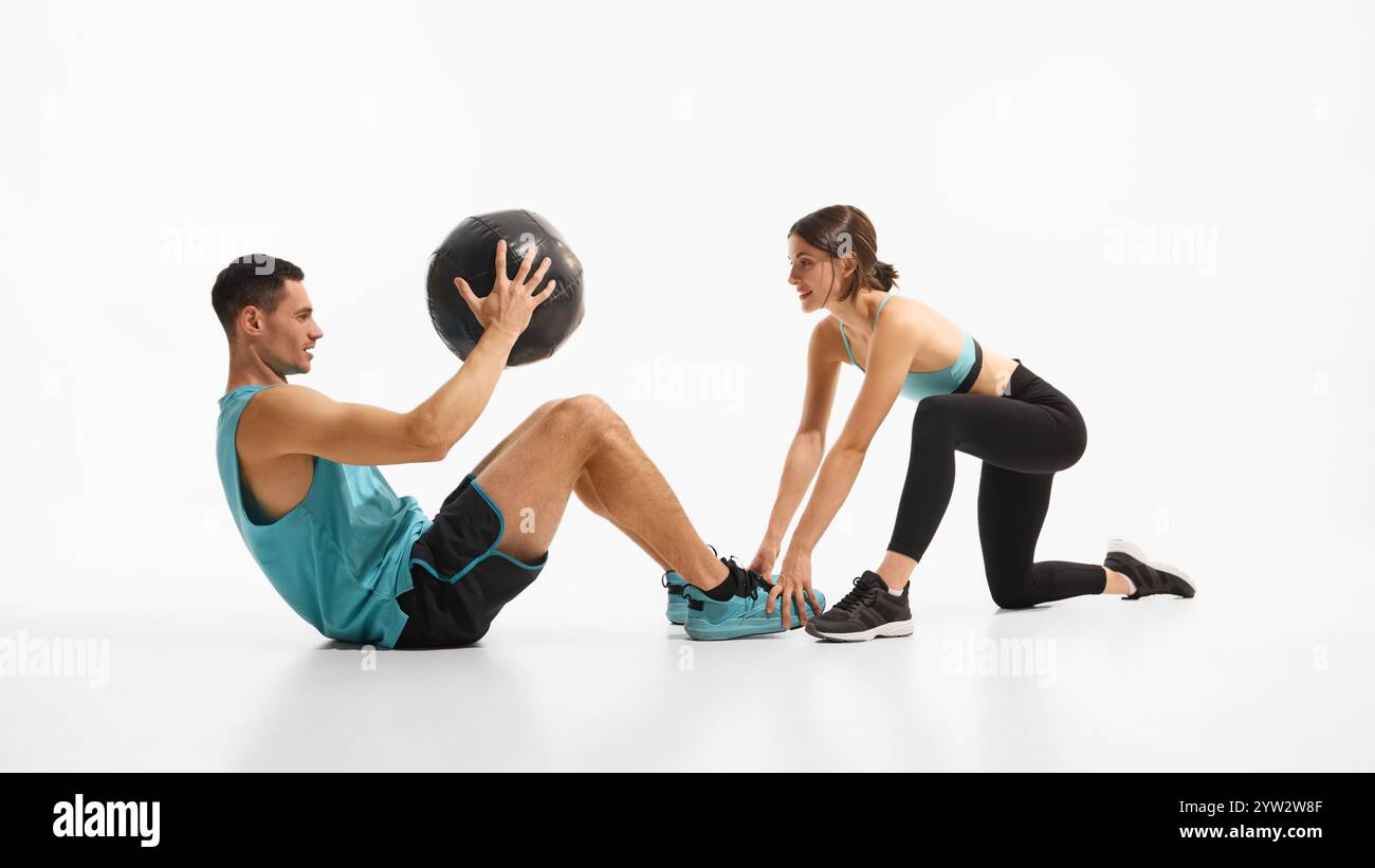 Muscular young man doing abs exercises with medicine ball while woman ...