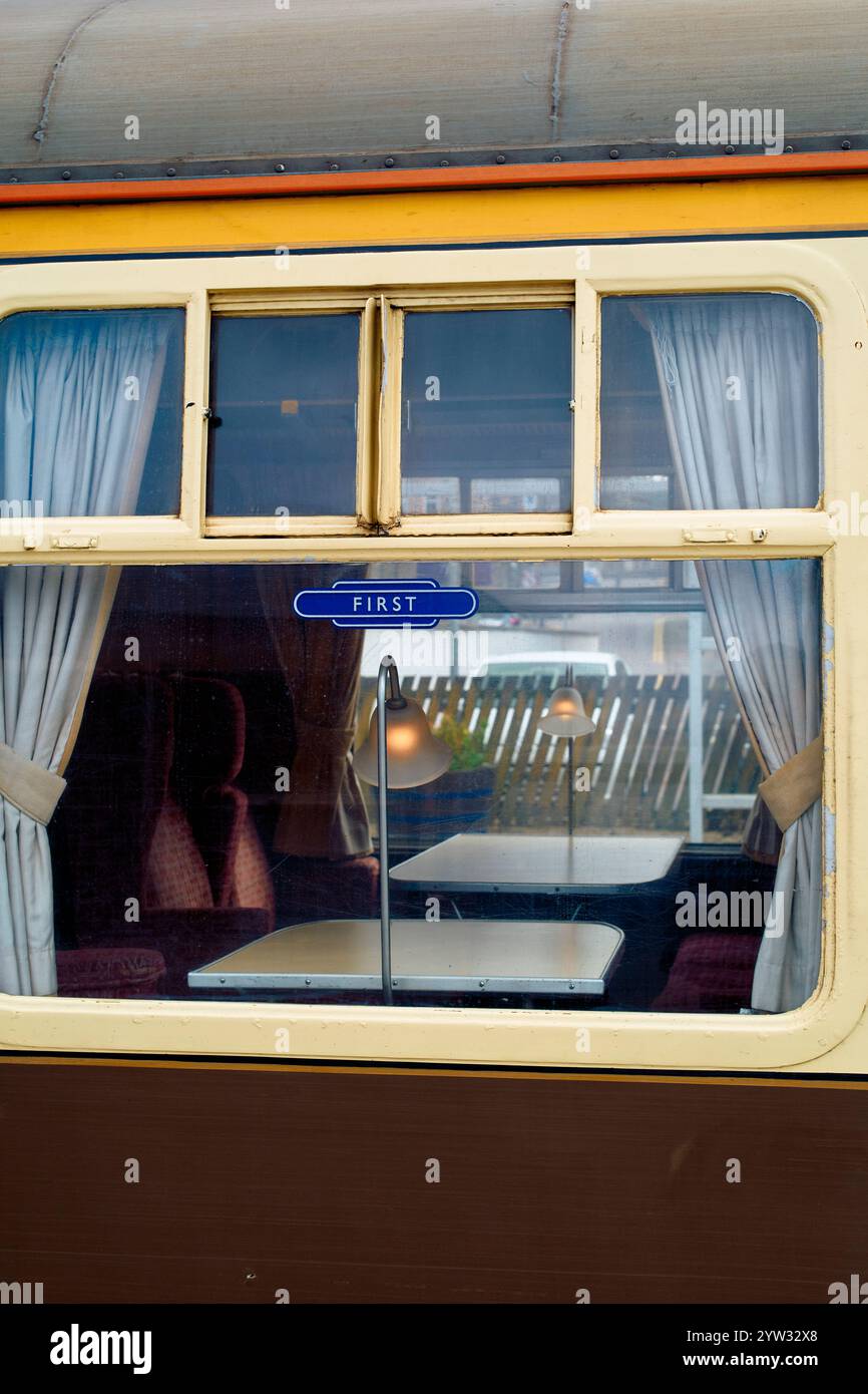 Vintage train carriage window with a First'class sign, showing plush seating and curtains inside, Scotland Stock Photo