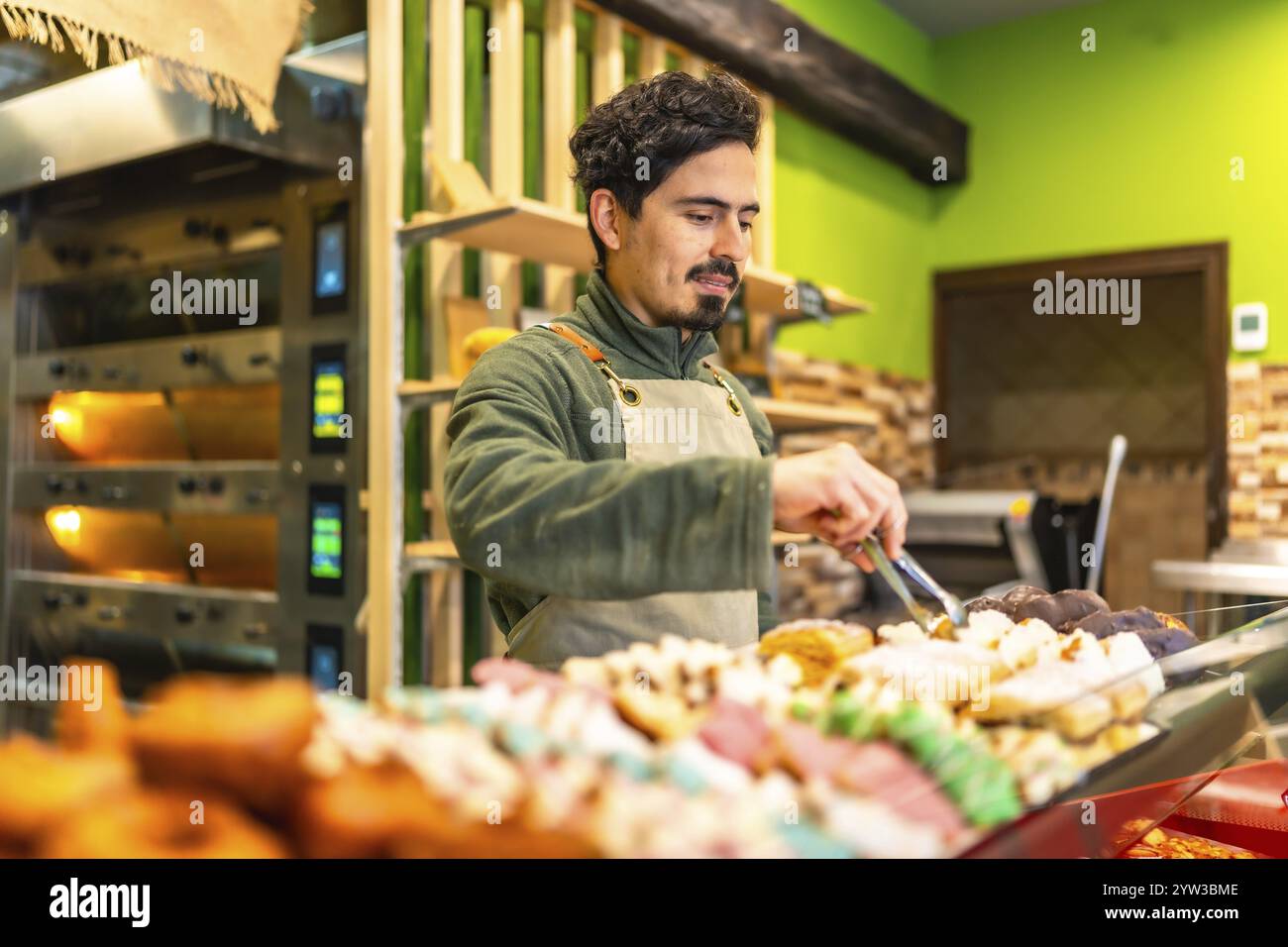 Backer Shop Latin young male baker arranging pastries on the counter of an artisan ...