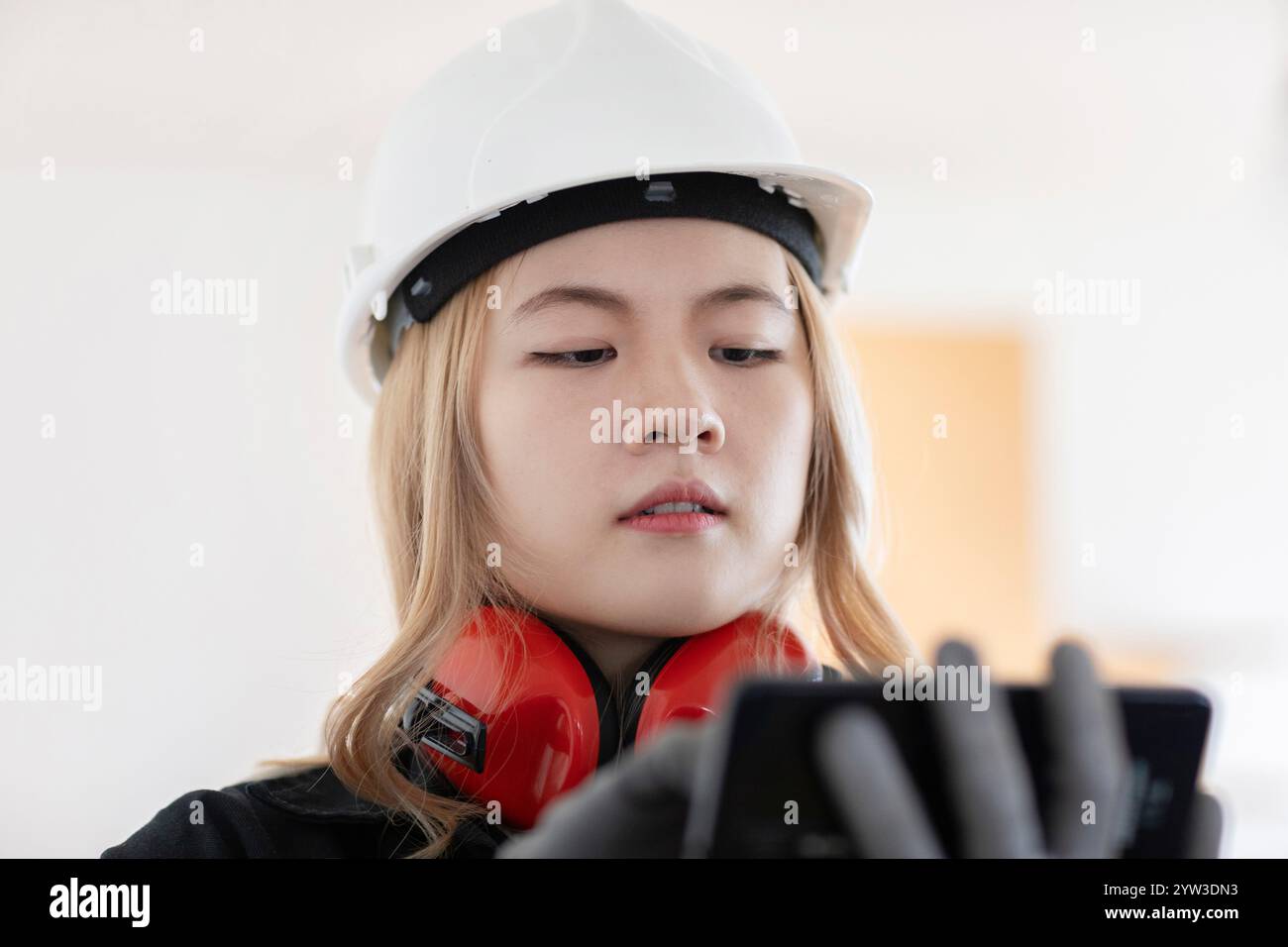 Construction worker in a white hardhat and earmuffs using a smartphone. Stock Photo