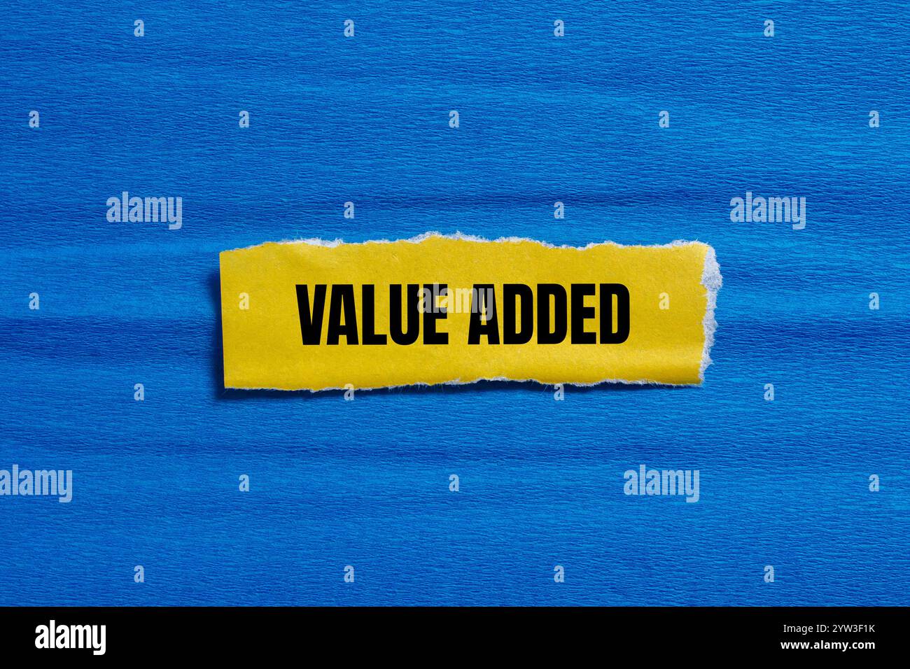 Value added message written on ripped torn yellow paper piece with blue ...