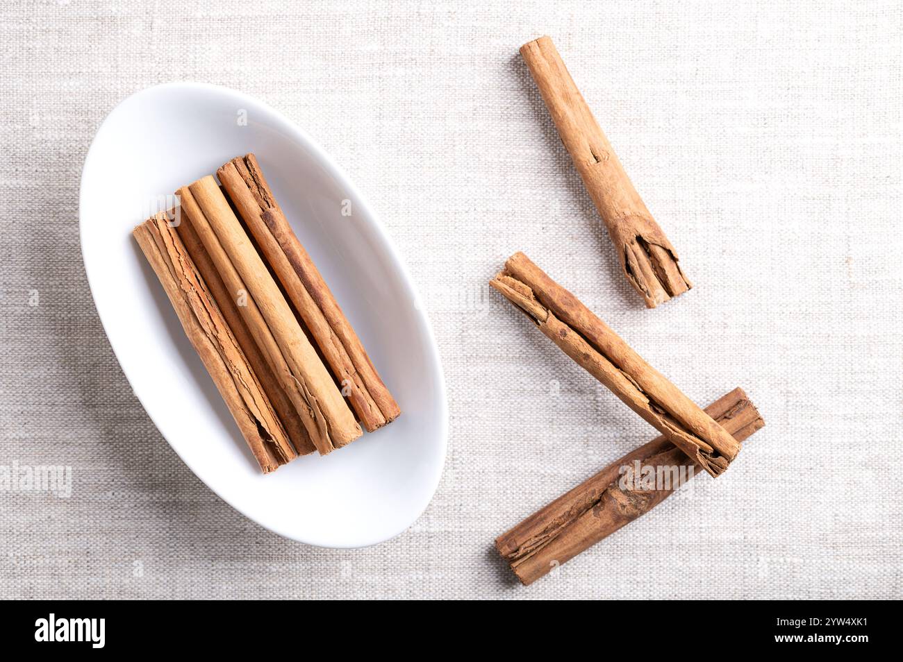 Ceylon cinnamon sticks, cinnamon quills in an oval white bowl on linen. Group of whole dried bark strips of Cinnamomum verum. Stock Photo