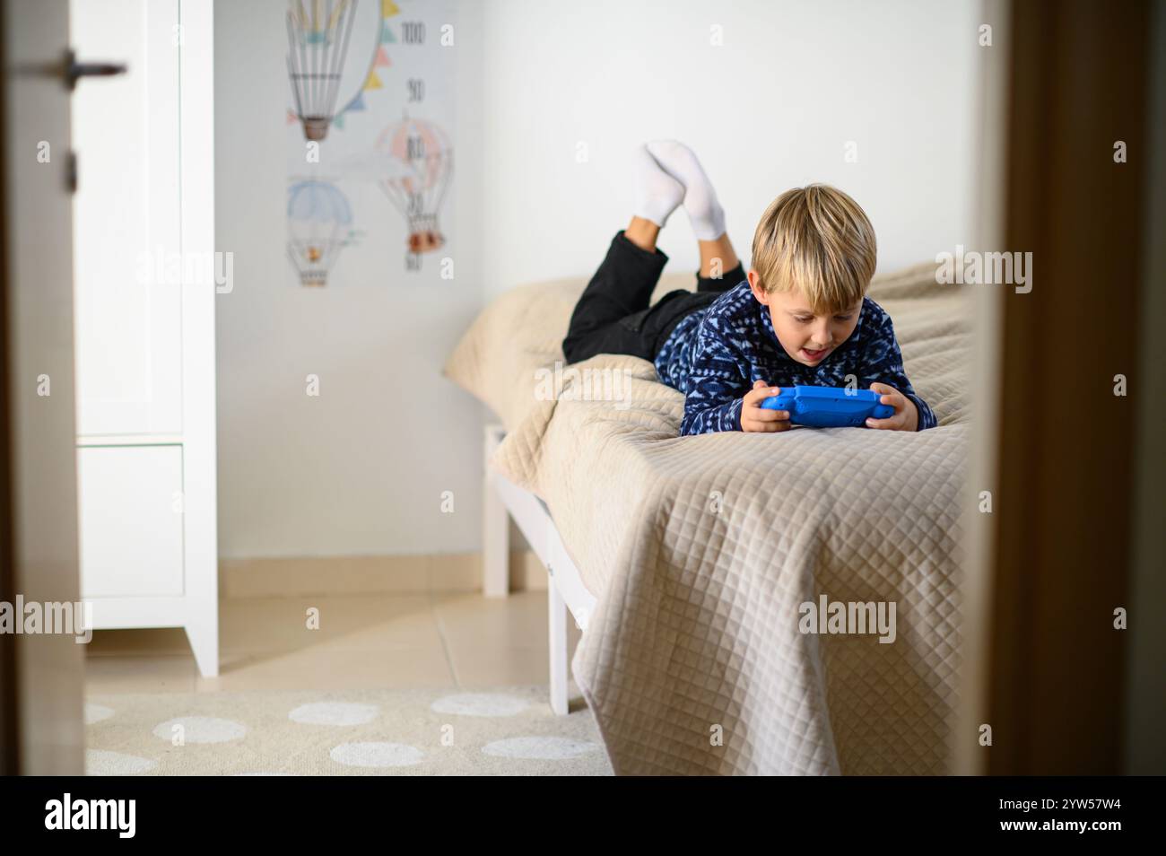 a boy is lying on a bed in a children's room and playing video games ...