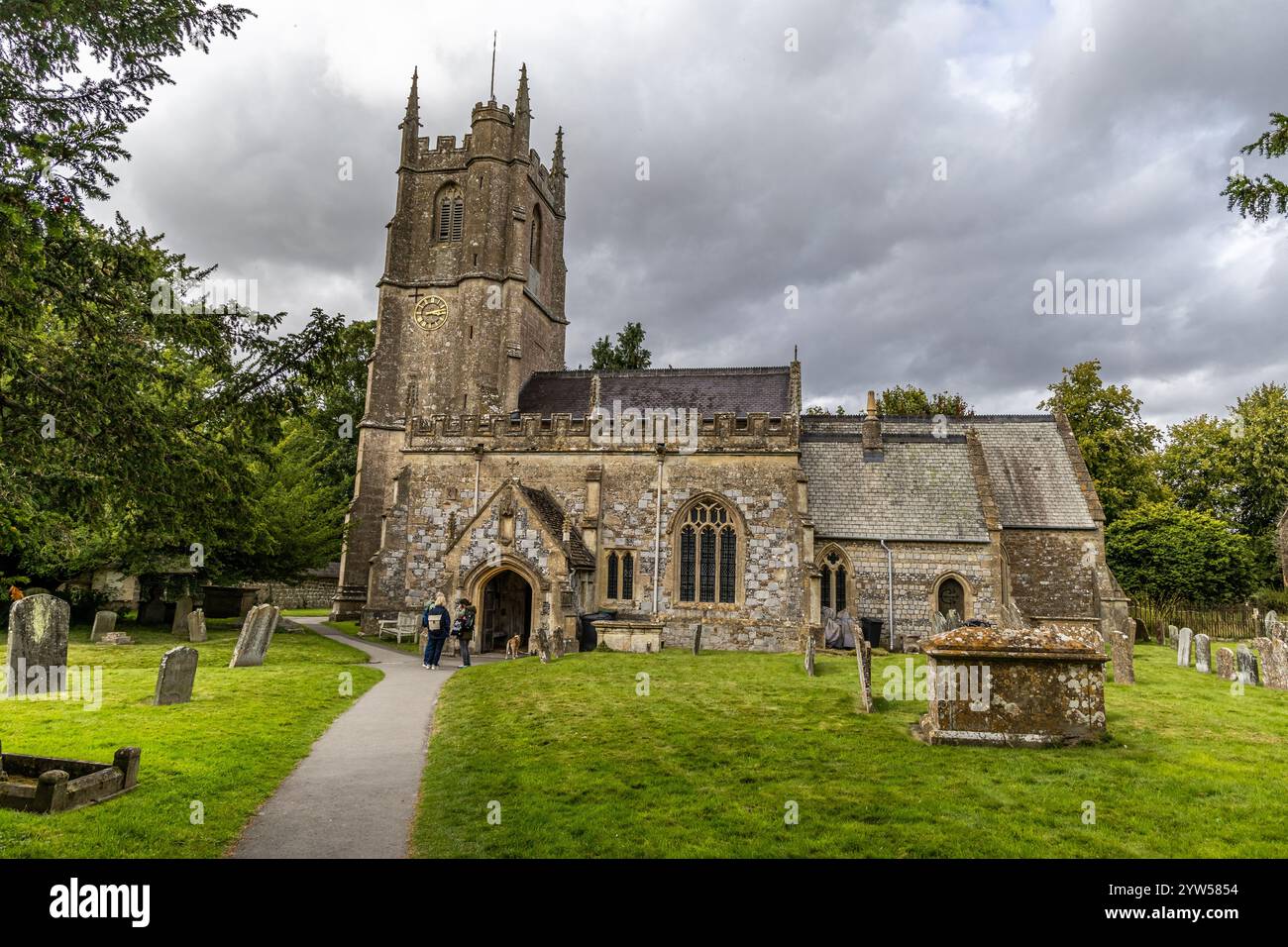 Avebury, UK- August 25, 2024: Avebury Church dates from the year 1000 AD and is situated near Avebury Manor in Wiltshire. a woman sits on a bench besi Stock Photo