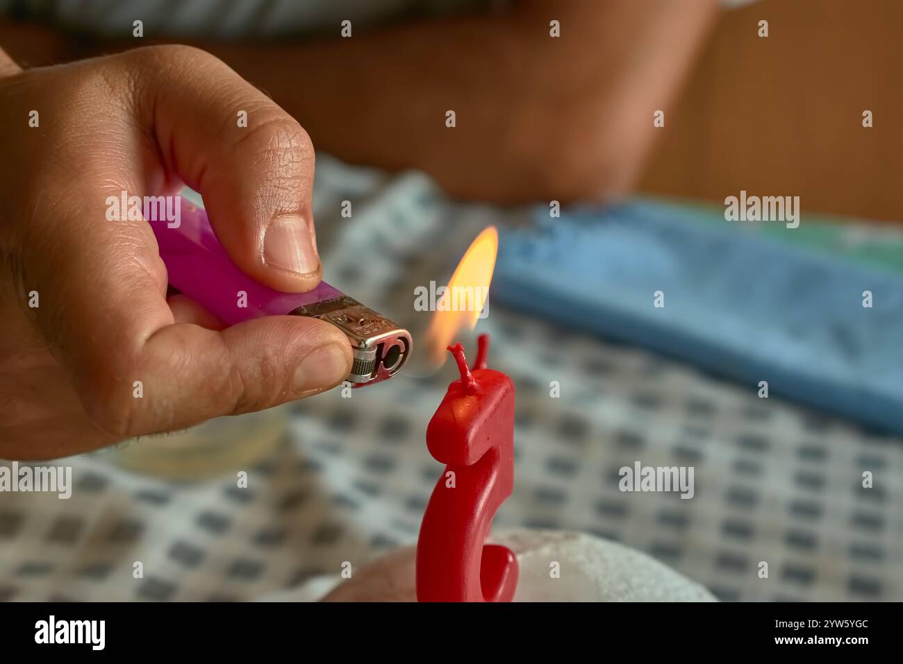 A close-up of a hand holding a lighter as it ignites a candle shaped like the number 5. The image captures a celebratory moment Stock Photo