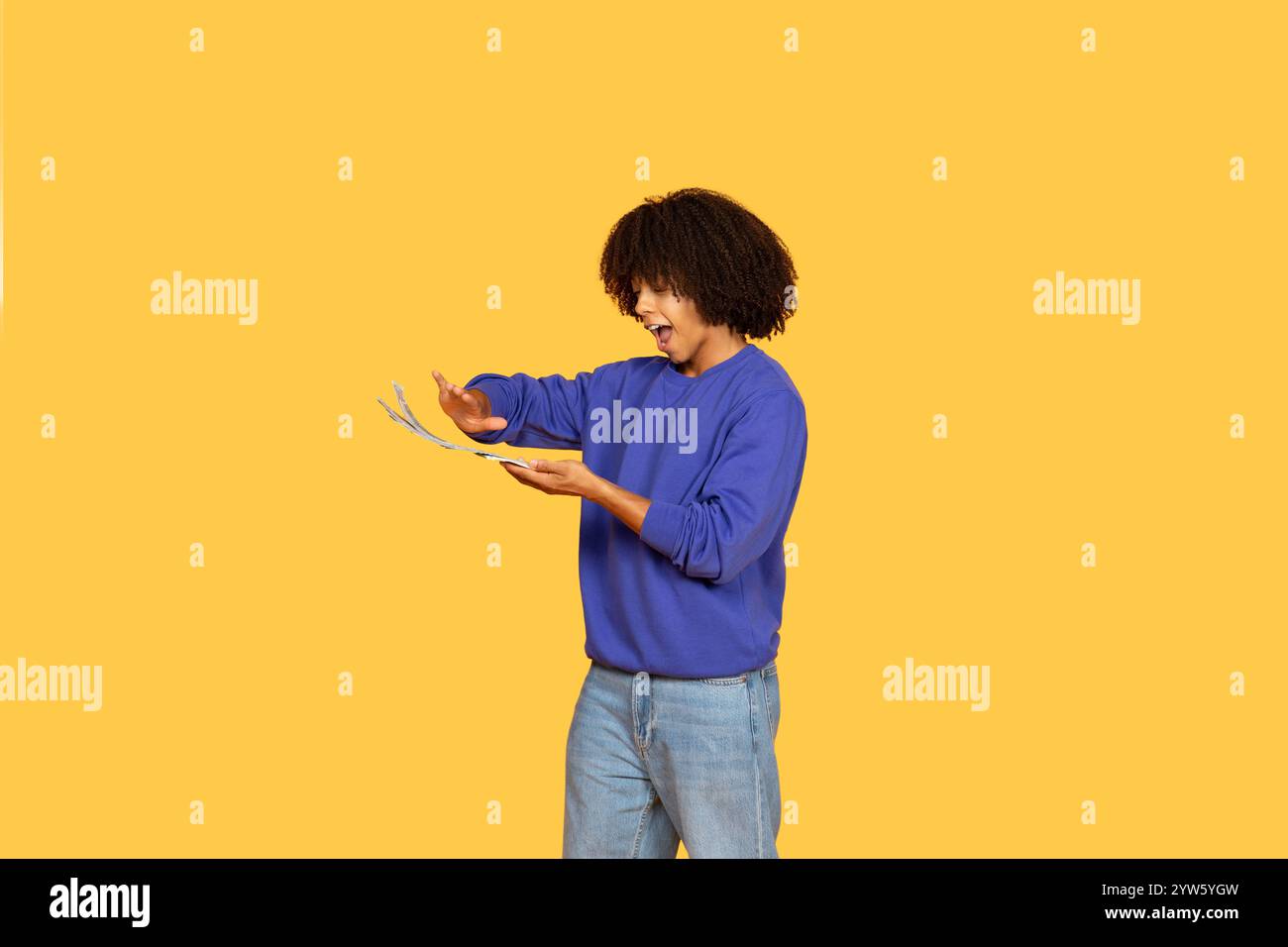 Young man with curly hair expressing excitement while engaging with money Stock Photo