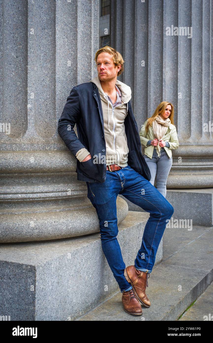Two people are standing near large stone columns, with the man in the foreground leaning slightly against the structure and the woman in the backgroun Stock Photo