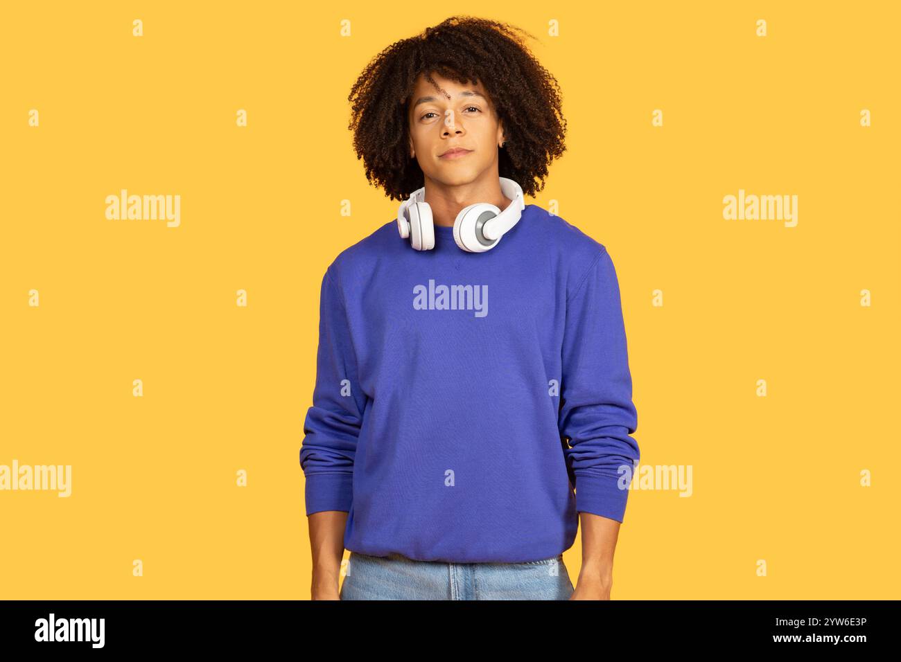 Young man with headphones stands confidently against a bright yellow backdrop Stock Photo
