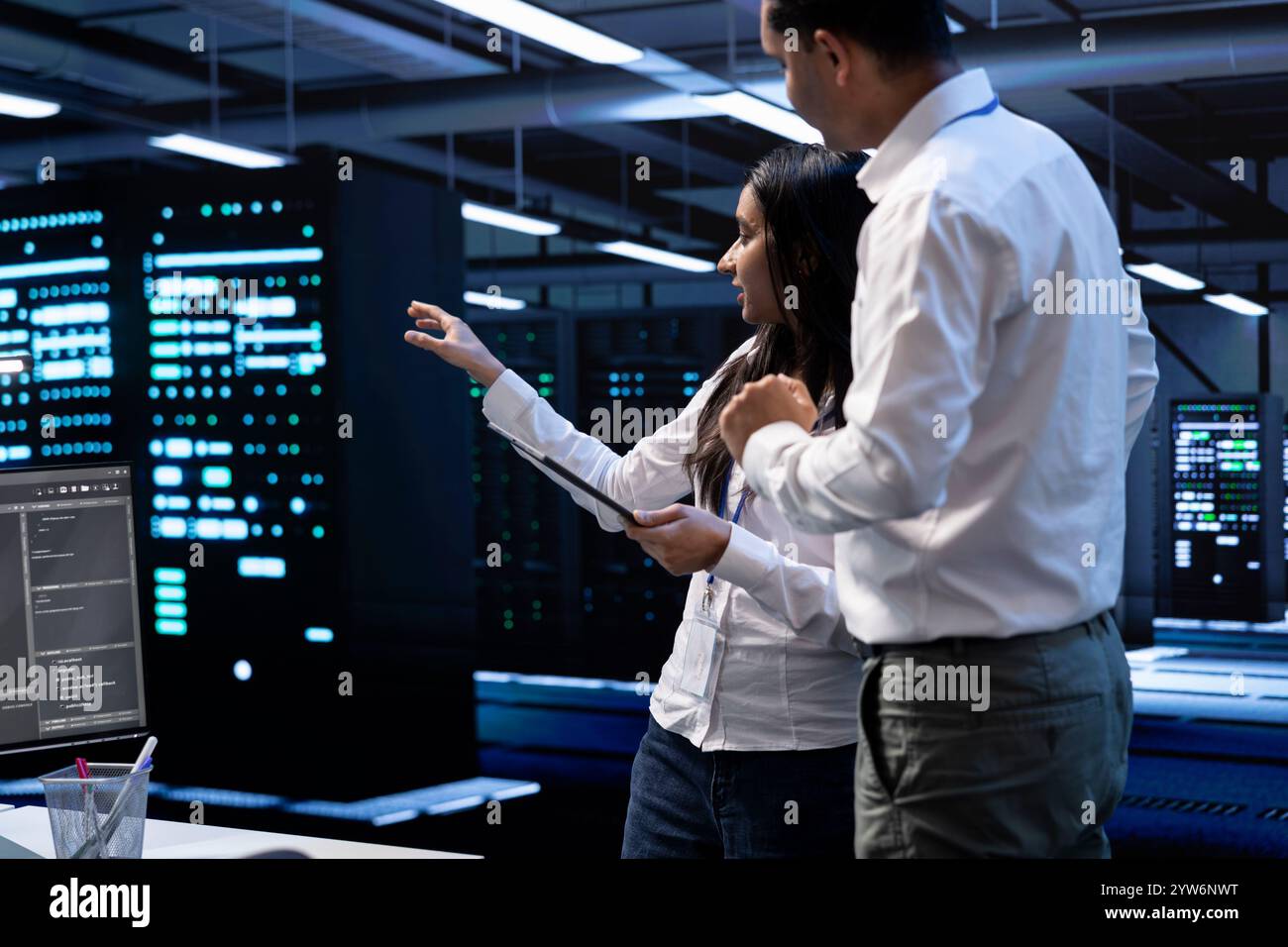 Engineering colleagues in data center looking for firewall misconfigurations affecting servers, doing brainstorming. System administrators in server room checking systems bottlenecks Stock Photo