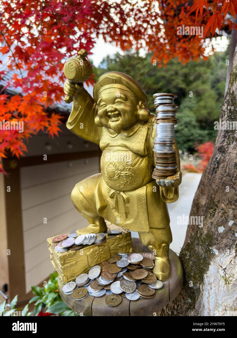 Ebisu Statue with Coins Under Vibrant Autumn Leaves Stock Photo