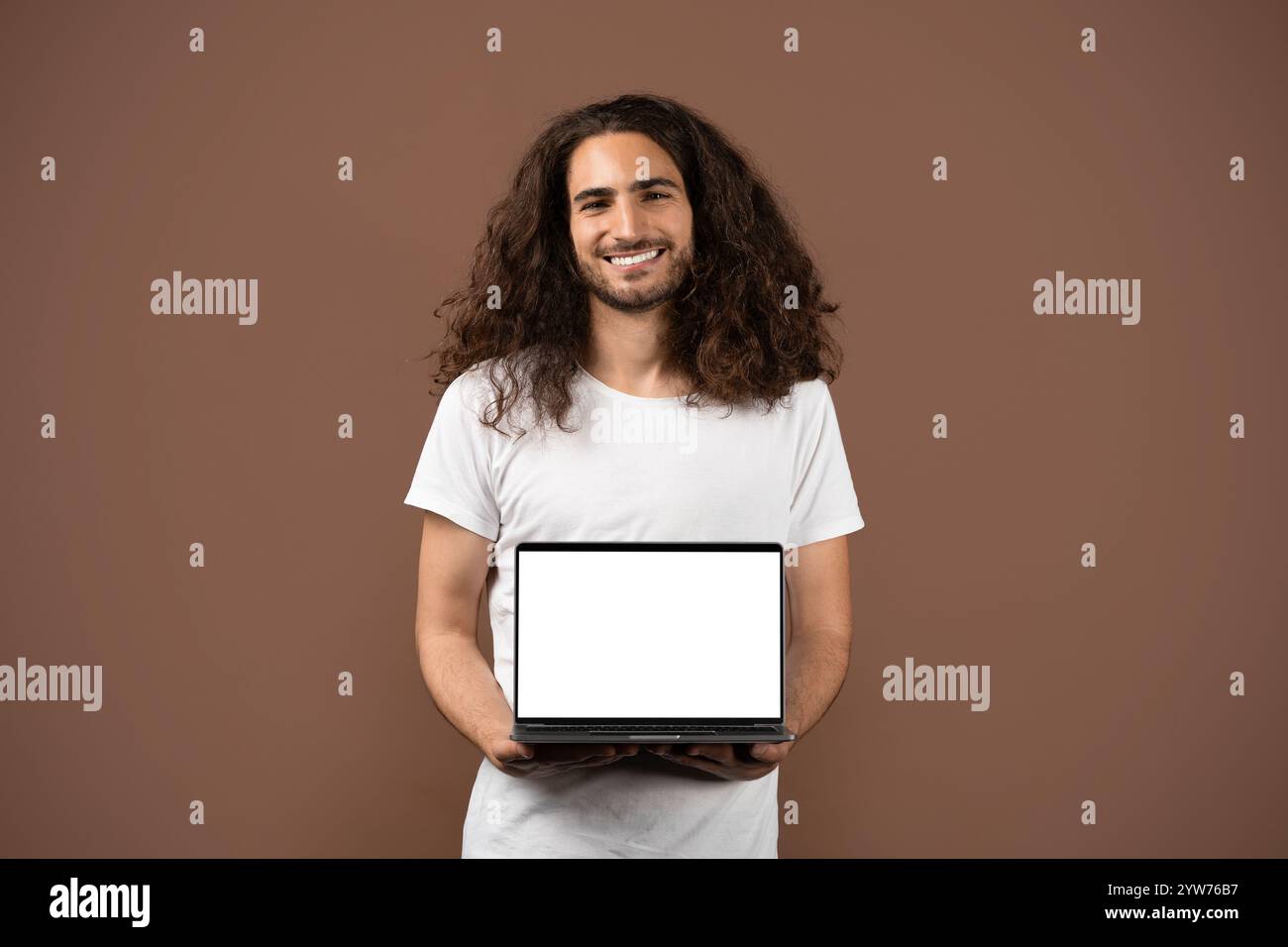 Confident young man with curly hair poses with a laptop Stock Photo