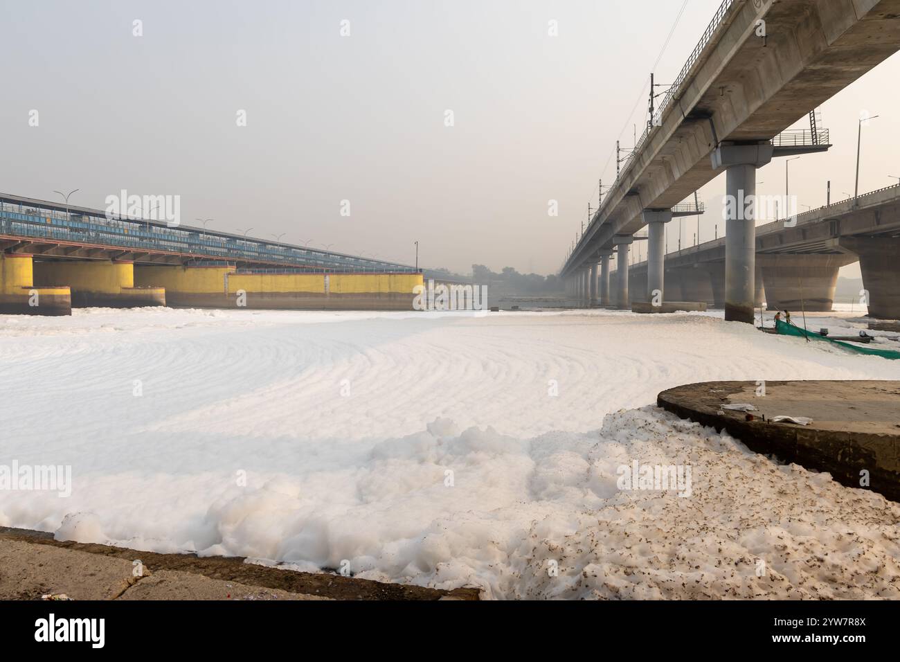 polluted river with industrial and domestic effluents toxic foam and road bridge at morning image is taken at yamuna river okhla barrage delhi india. Stock Photo
