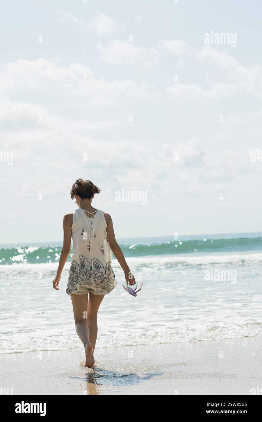 Back view of a woman in her 20s walking on a sandy beach Stock Photo ...