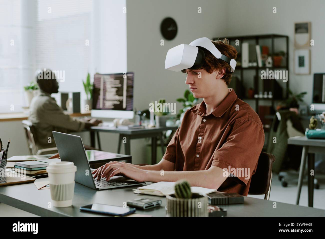 Caucasian man with VR headset sitting at work desk and programming, he focused on process Stock Photo