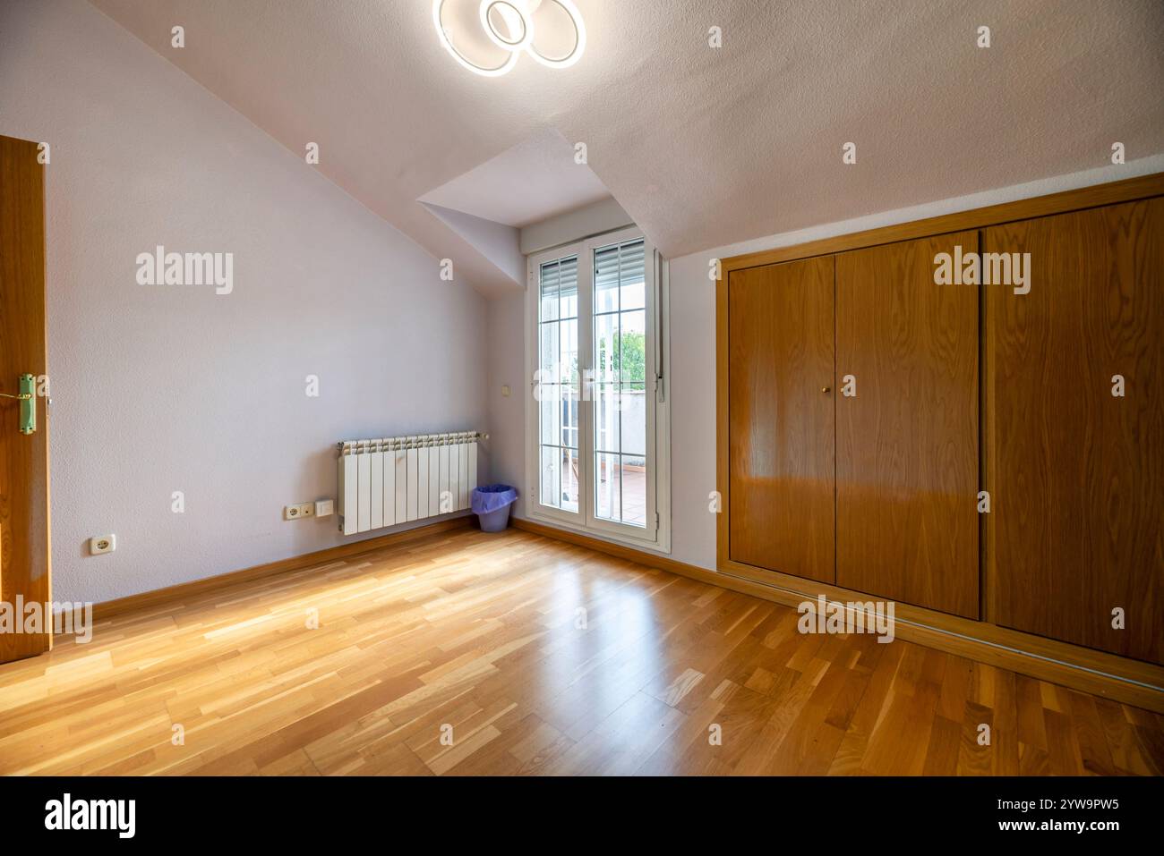 A bedroom in an attic room with custom-made wooden built-in wardrobes and a window leading out ...