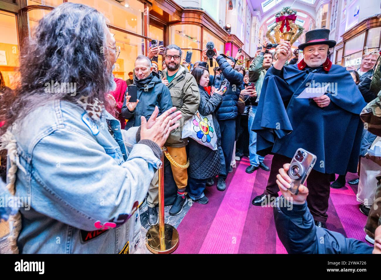 London, UK. 10 Dec 2024. Fans queue at teh shop to buy a t-shirt as the artist arrives and is welcomed by a bell ringing top hatted security guard - - Japanese Art History à la Takashi Murakami an new exhibition by Takashi Murakami, his largest show in London in 15 years, at Gagosian Grosvenor Hill, London. It offers his own reinterpretations of some of the most important artworks in Japanese art history, combining AI-generated images with hand painted elements. He also took over the Gagosian Gallery Shop in Burlington Arcade to release two hundred limited-edition T-shirts designed by the arti Stock Photo