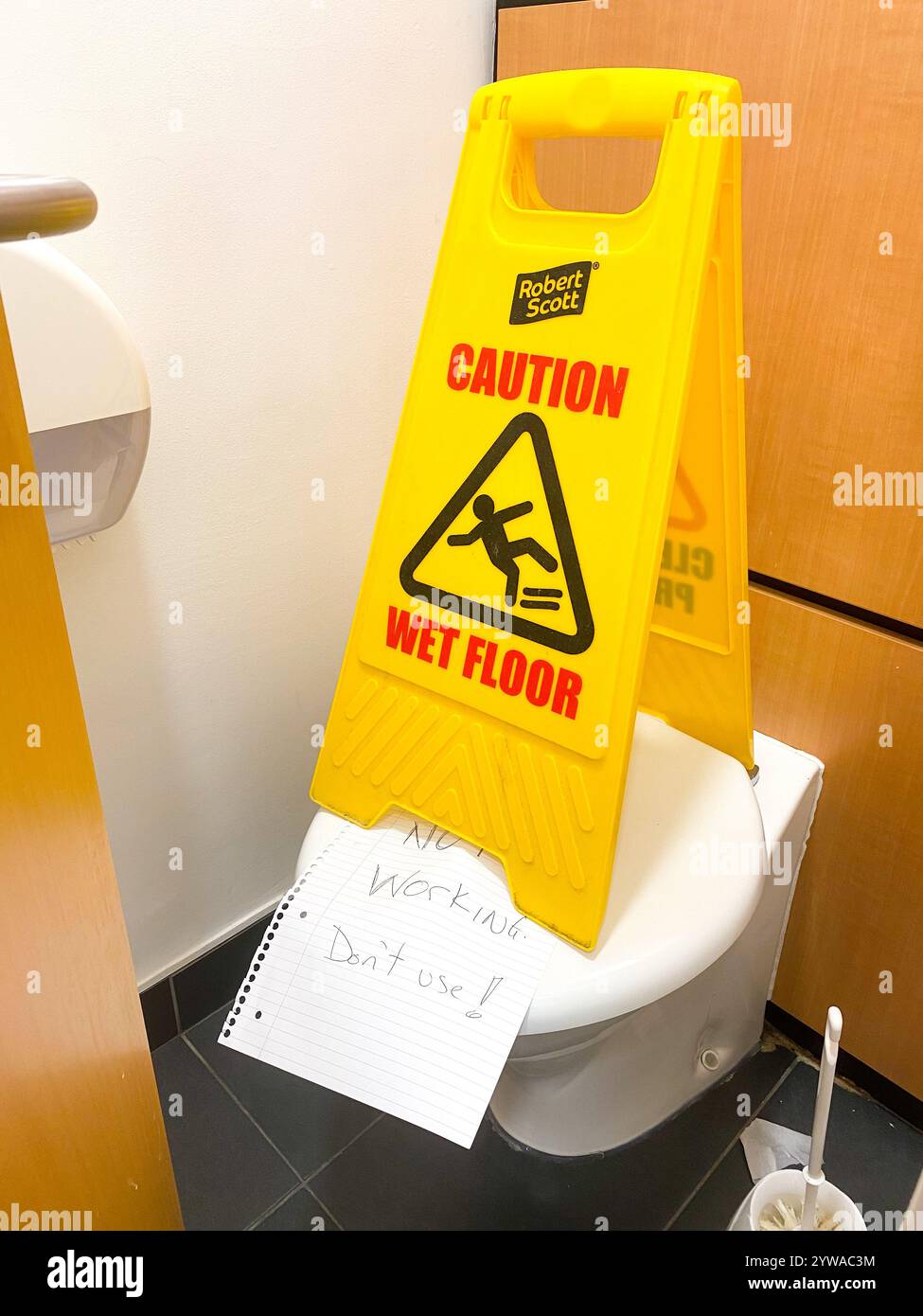 A wet floor is placed on top of a toilet in a cubicle along with a handwritten note stating that the toilet is not working. Stock Photo