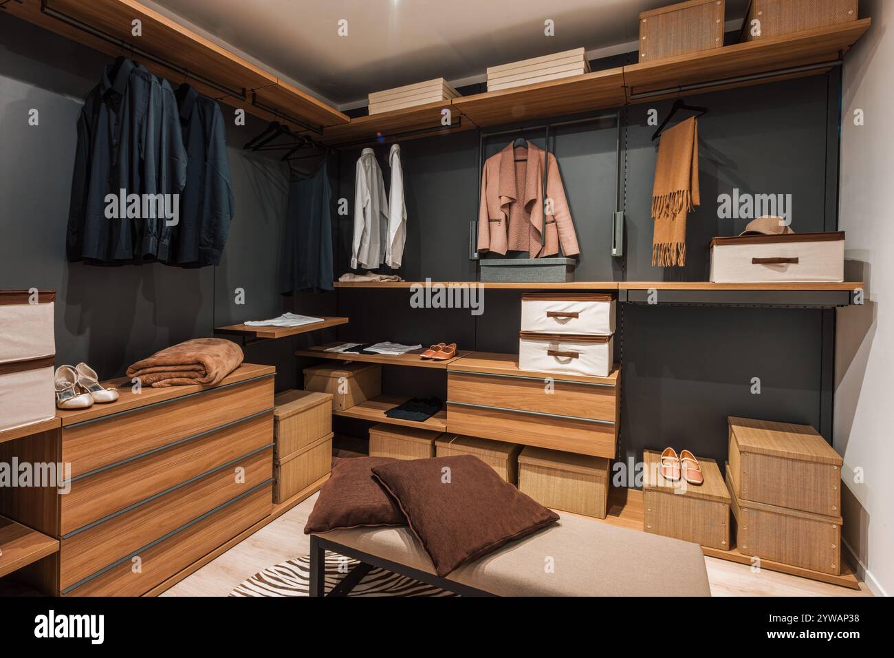 Interior of a modern and spacious walk in closet featuring wooden shelves, drawers, and organized clothing, shoes, and accessories Stock Photo