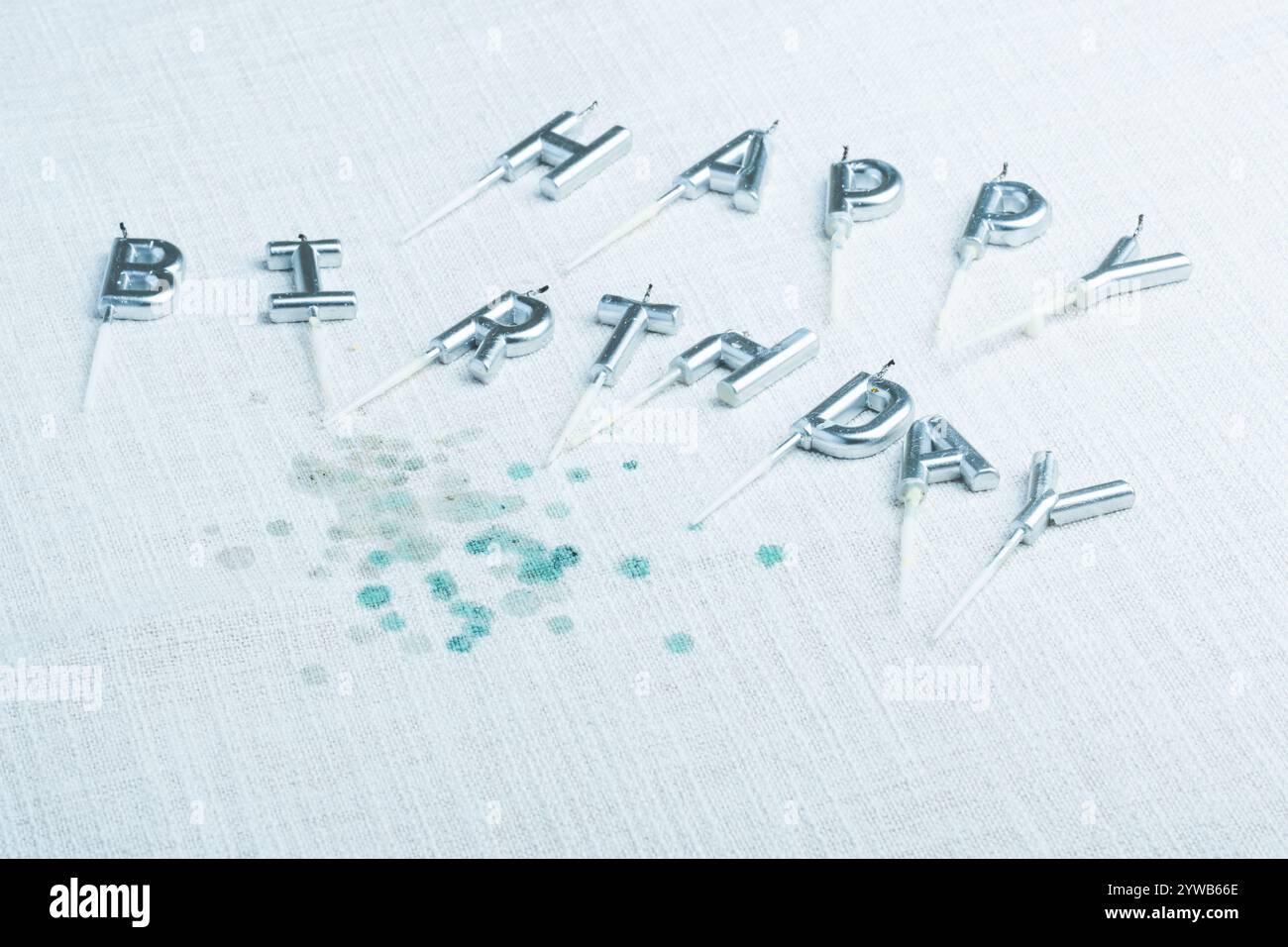 Silver letter candles spelling out Happy Birthday placed on a textured tablecloth with candle wax remnants. Celebrating a joyful birthday. Stock Photo