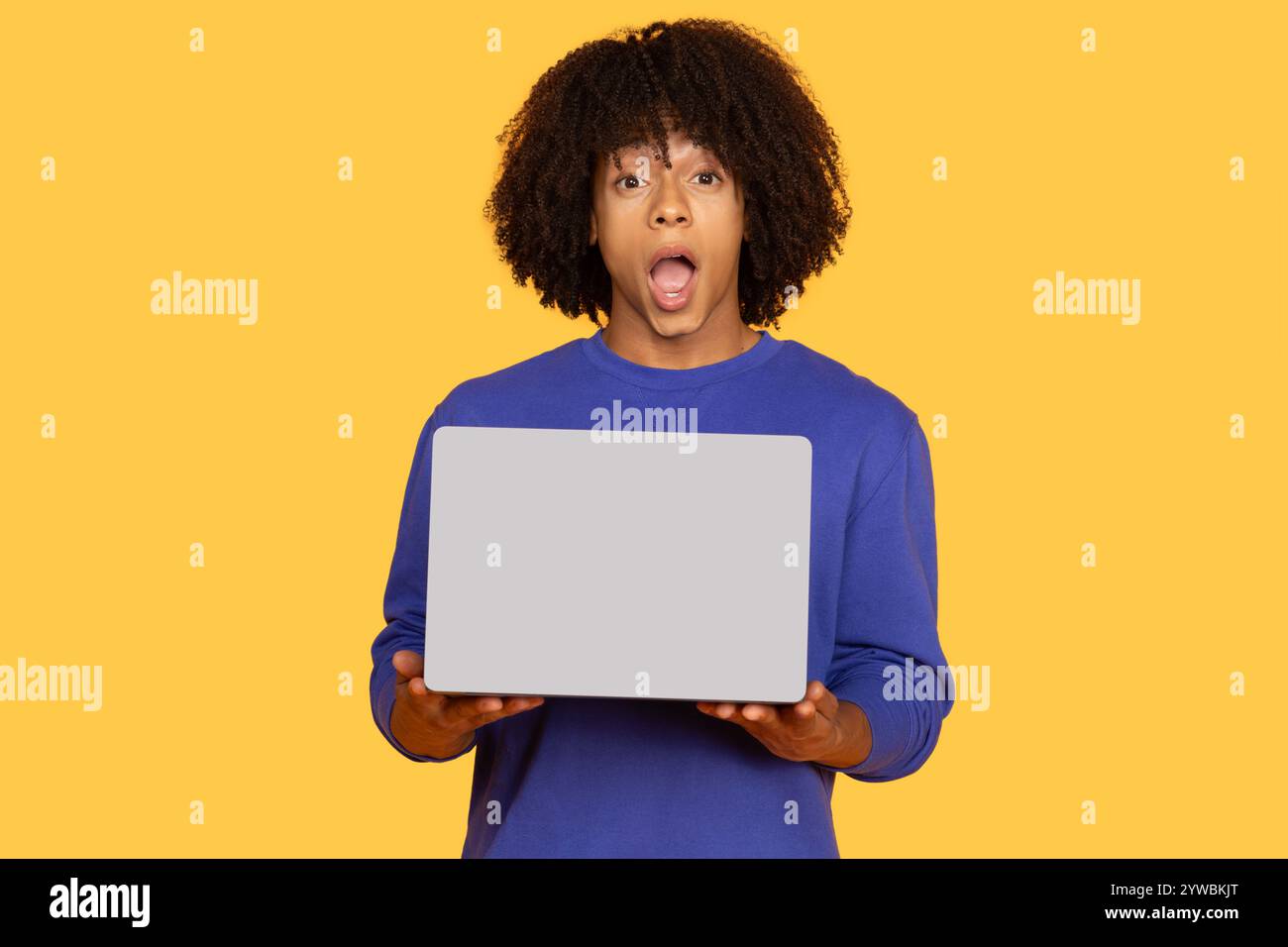 Young man surprised using a laptop on a bright yellow background Stock Photo