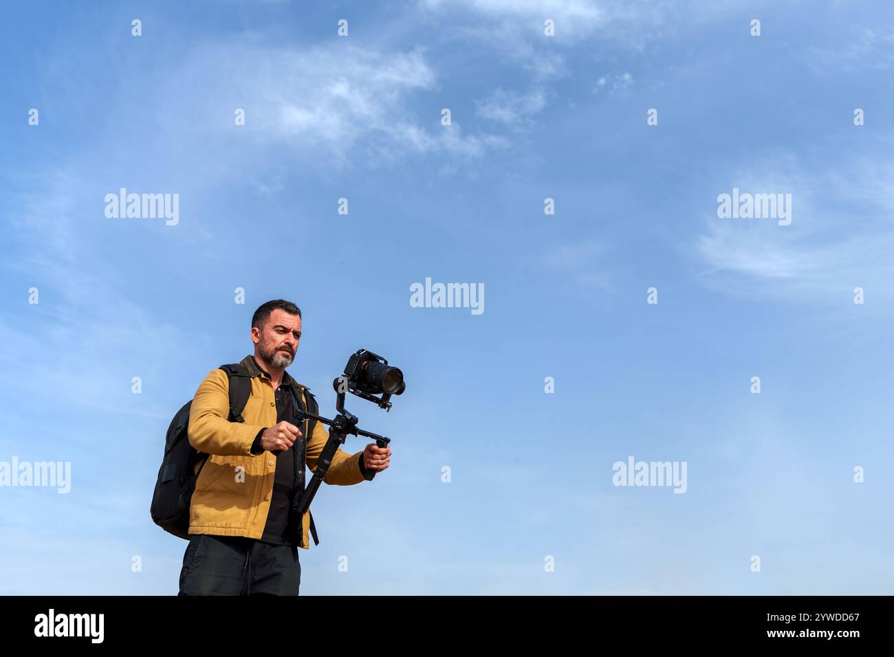 Videographer capturing breathtaking footage with a gimbal and camera against a picturesque partly cloudy blue sky, highlighting the craft of outdoor f Stock Photo