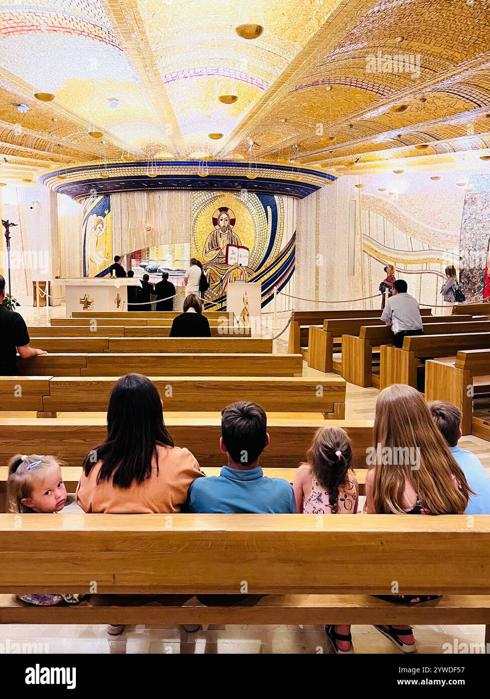 A family sits in a beautifully decorated chapel, observing a church service. The ornate and brightly lit interior adds to the spiritual ambiance. San Stock Photo