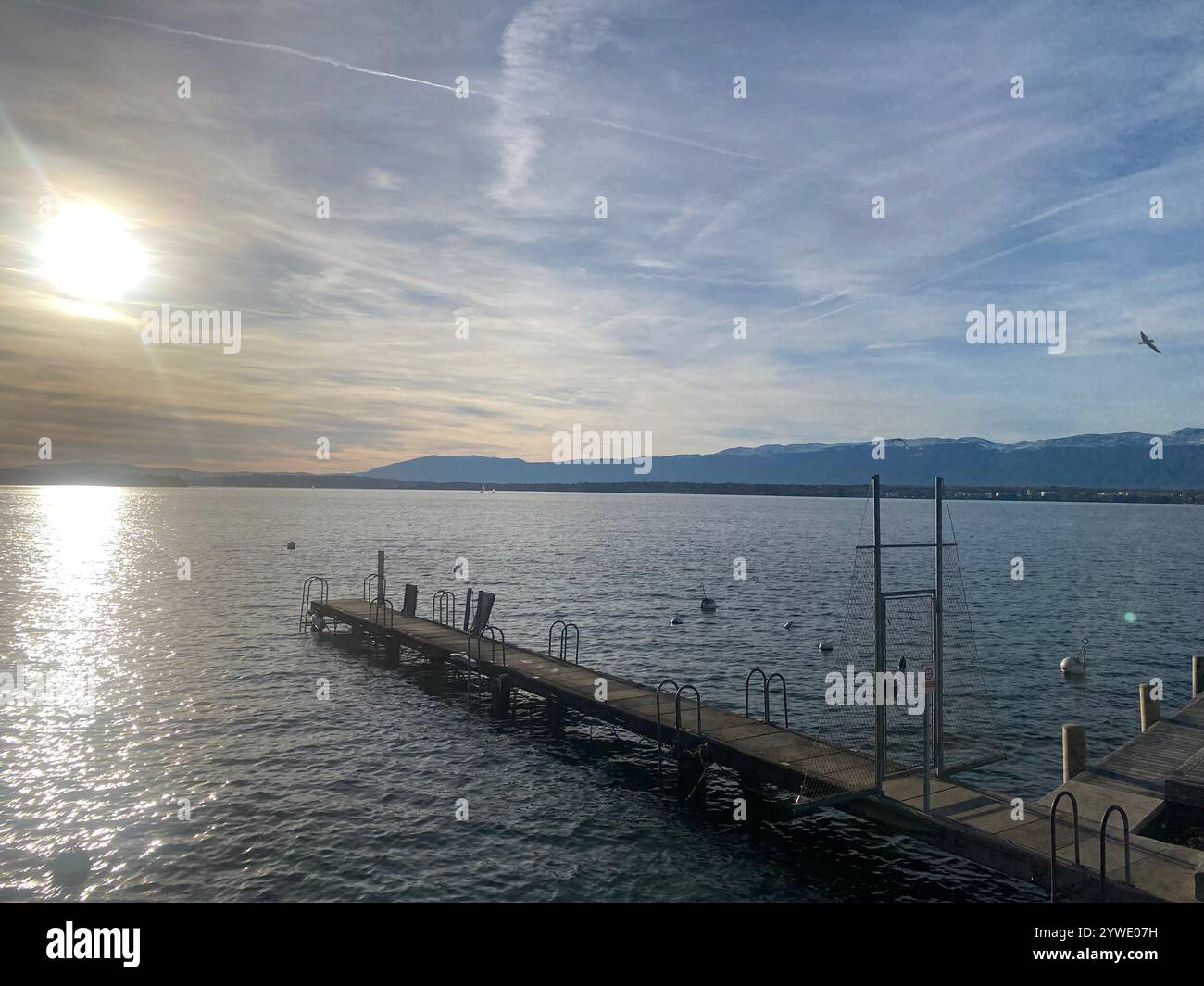 Beautiful sunset over calm waters with a wooden pier and distant mountains on a peaceful day - Smartphone Captured Stock Image