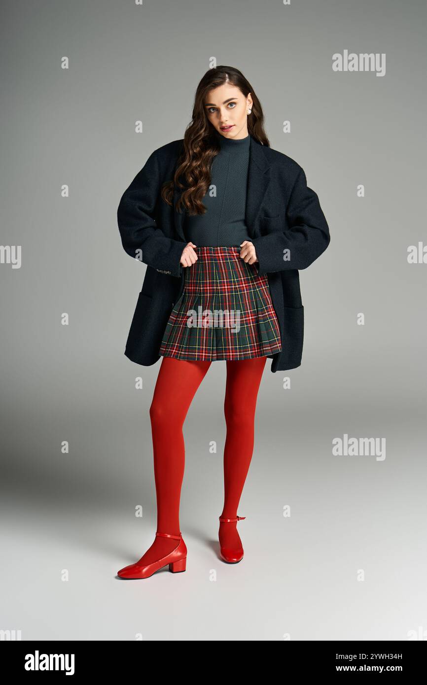 Pretty young woman poses confidently in a fashionable outfit against a neutral backdrop. Stock Photo