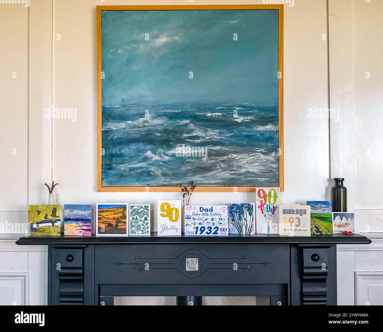 A fireplace and mantelpiece with 90th birthday celebration cards to a father displayed and a seascape painting, UK Stock Photo