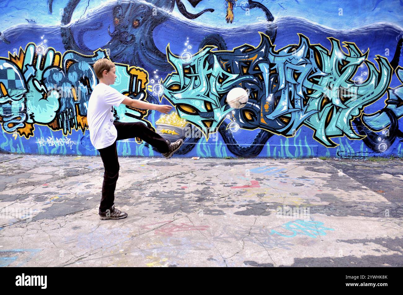 A ten-year-old boy plays with his football in front of a graffiti wall, football pitch in Germany Stock Photo