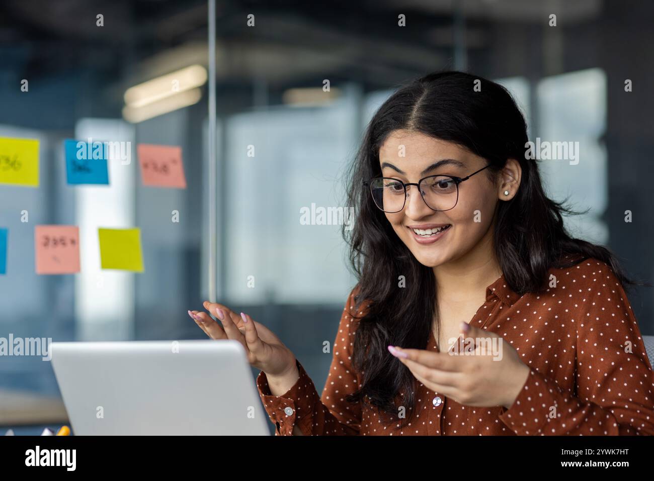 Businesswoman communicating during an online meeting, utilizing technology for effective collaboration. She is surrounded by notes, focusing on professional tasks in a modern office Stock Photo