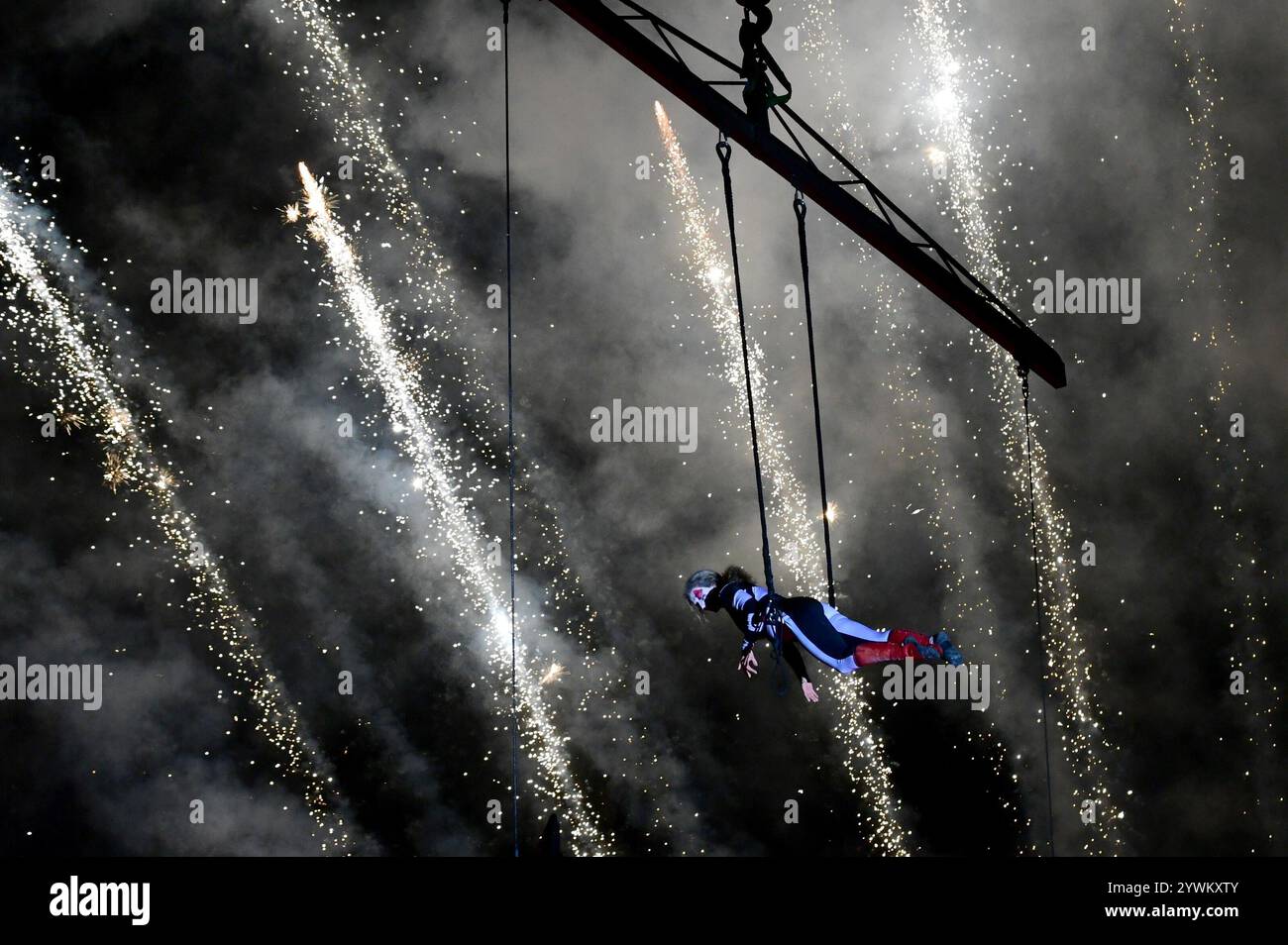 An acrobat performs figures in flight in front of a fireworks display ...
