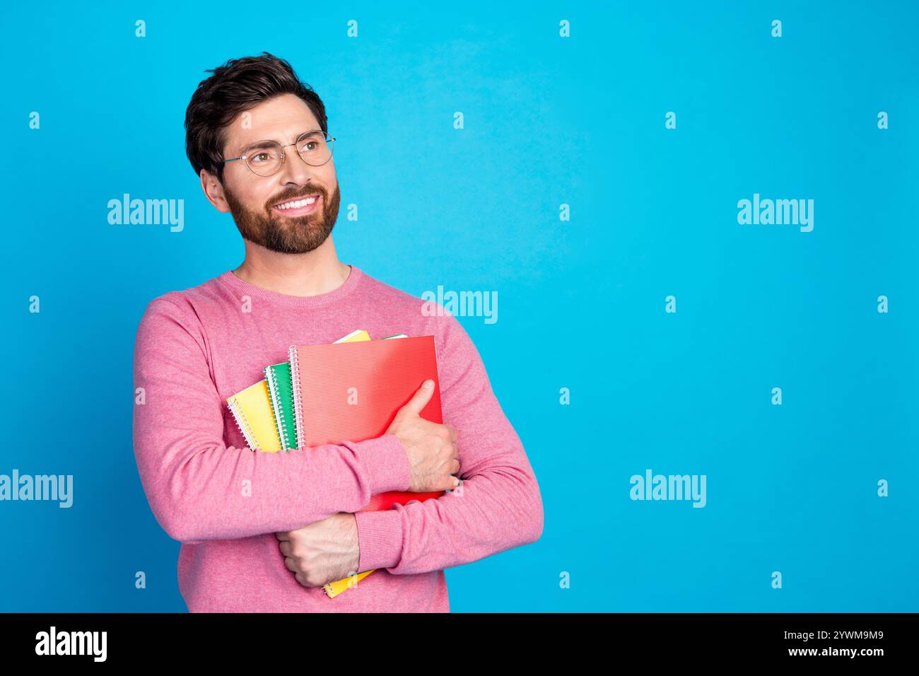 Confident man holding colorful notebooks against blue background, expressing thoughtful and cheerful mood Stock Photo