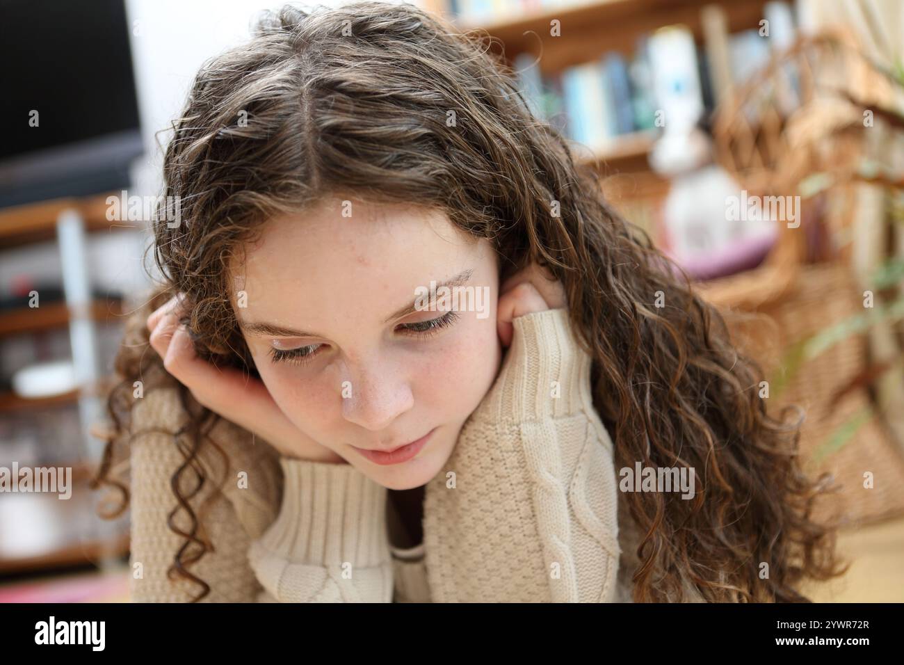 Teenage girl lying on floor with hands on face propped up hands under chin curly hair Stock Photo