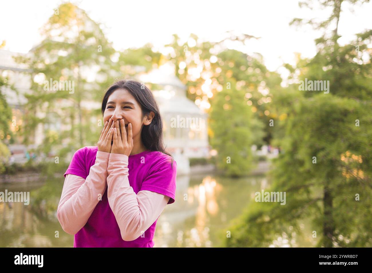 Peruvian student enjoying a day at el retiro park in madrid, covering her mouth while laughing Stock Photo