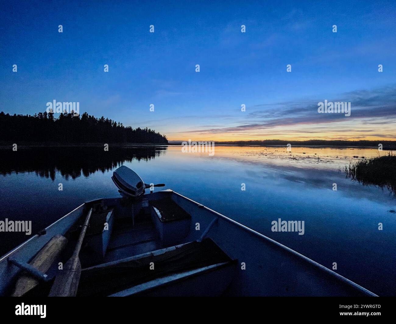 A tranquil boat gliding across a calm lake at sunset, with the boat's silhouette reflected on the water, surrounded by lush greenery and a warm, gold - Smartphone Captured Stock Image